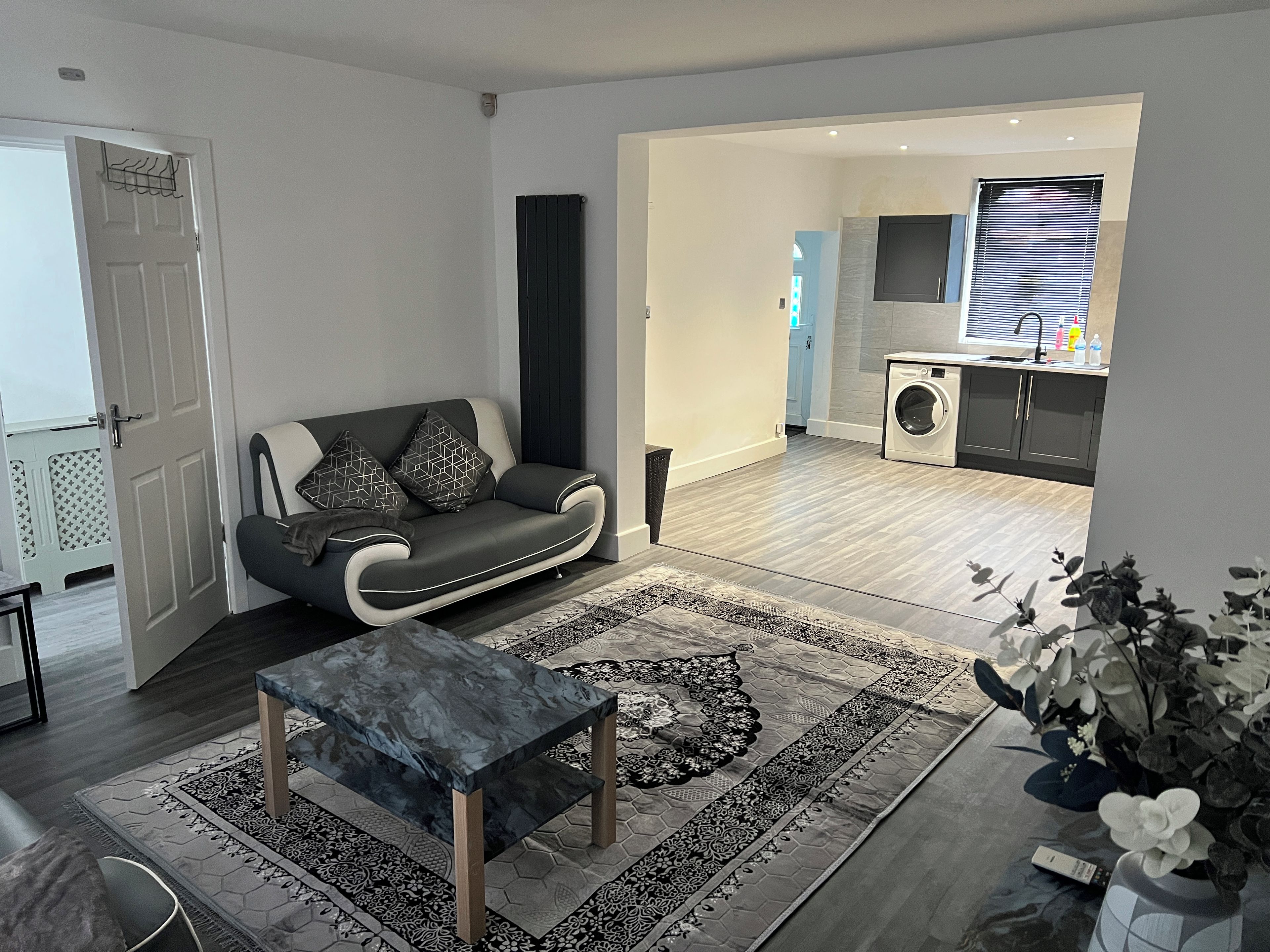 A modern living room with a sofa, coffee table, and a view into the kitchen area.