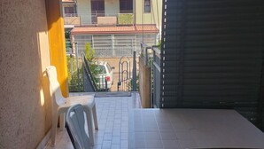 Un balcon avec une table et des chaises, une vue sur un immeuble avec un toit en tuiles et une voiture garée.