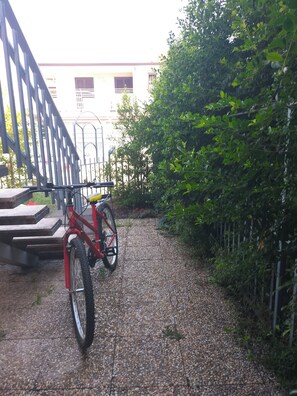 Een rode fiets geparkeerd op een grindpad, met een metalen hek en beplanting aan de zijkant.