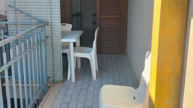 Un petit espace extérieur aménagé en patio, avec une table et des chaises, une porte en bois et une rambarde en métal.