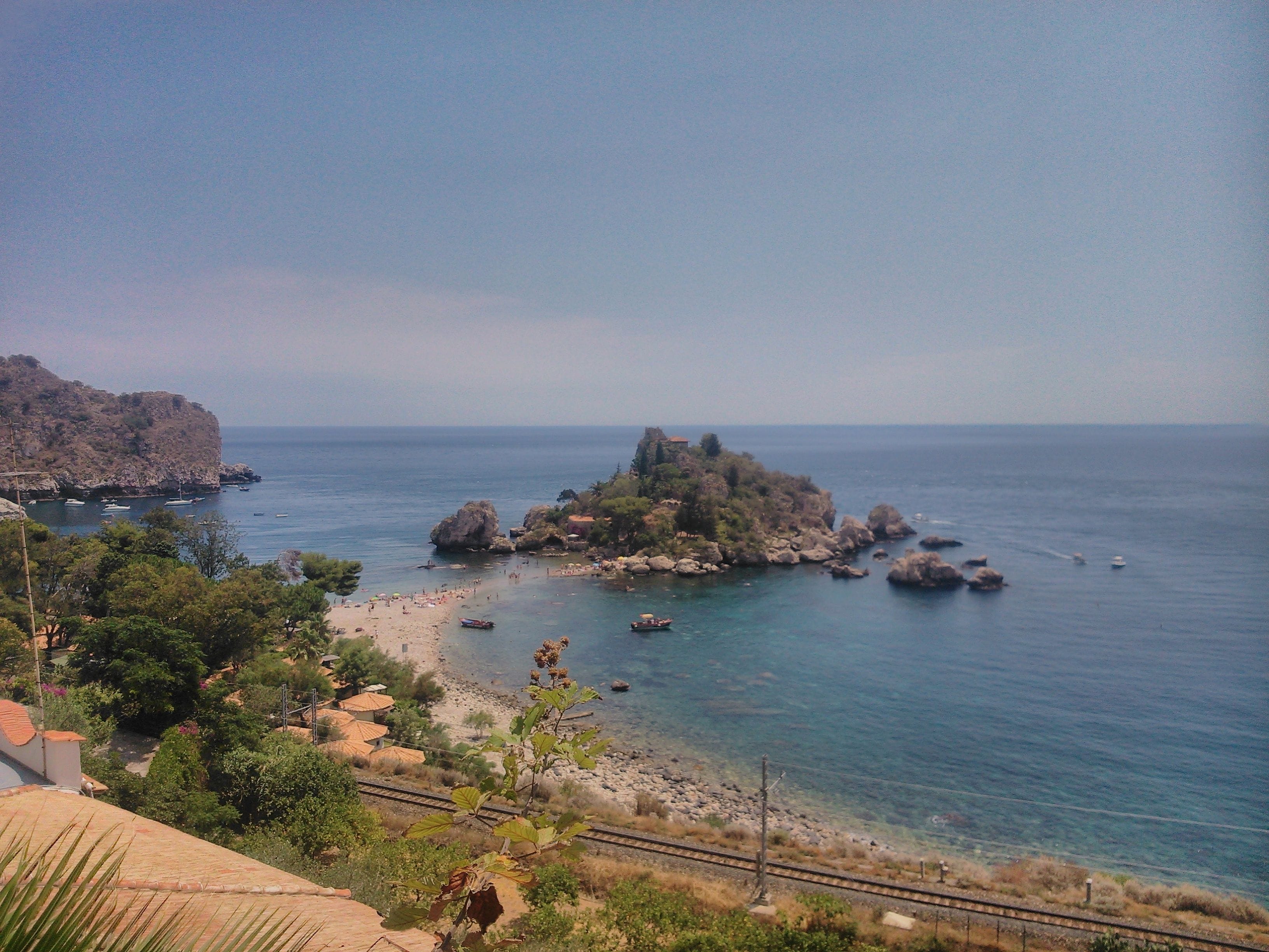 A coastal landscape with a rocky island, a beach, and a clear sky.