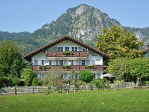 Ein zweistöckiges Hotel mit einem Balkon im zweiten Stock, umgeben von Grünpflanzen und einem Bergpanorama.