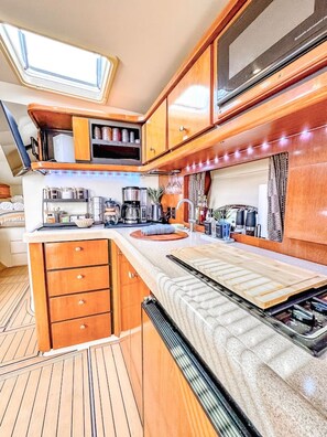 A compact kitchen with wooden cabinets, a countertop, and a built-in oven. - Waterfront Boat Stay & Resort Amenities (Key West)
