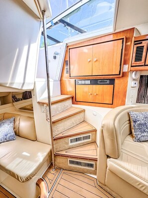 A compact interior with a wooden cabinet, a cushioned bench, and a small staircase. - Waterfront Boat Stay & Resort Amenities (Key West)