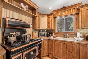 A kitchen with wooden cabinets, a stove, a microwave, and a window with a view of trees. - Bright Mountain Cabin with Private Fire Pit near Yellowstone in Island Park, Idaho (Island Park)