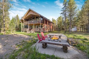 En hytte med terrasse, bålsted og røde Adirondack-stole.