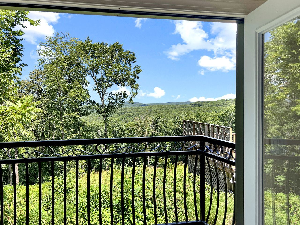 A balcony with a metal railing overlooking a lush green landscape and a clear blue sky.