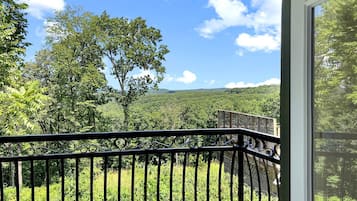 A balcony with a metal railing overlooking a lush green landscape and a clear blue sky.