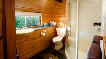 A wooden cabin bathroom with a sink, toilet, and glass shower enclosure.