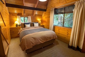 A wooden room with a bed, two bedside tables, and a window with curtains.
