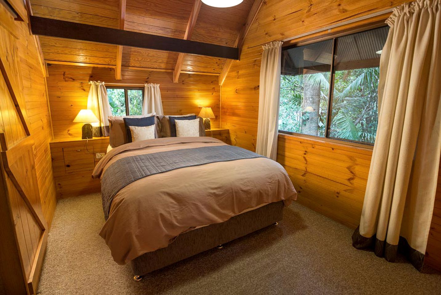 A wooden room with a bed, two bedside tables, and a window with curtains.