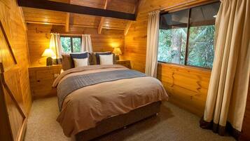 A wooden room with a bed, two bedside tables, and a window with curtains.