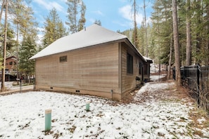 Eine Blockhütte mit schneebedecktem Dach, umgeben von Wald und einem Metallzaun.
