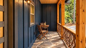 A covered porch with a stone floor, wooden railing, and a table with chairs. - Celastrina Cottage of Sapphire Valley (Jackson County)