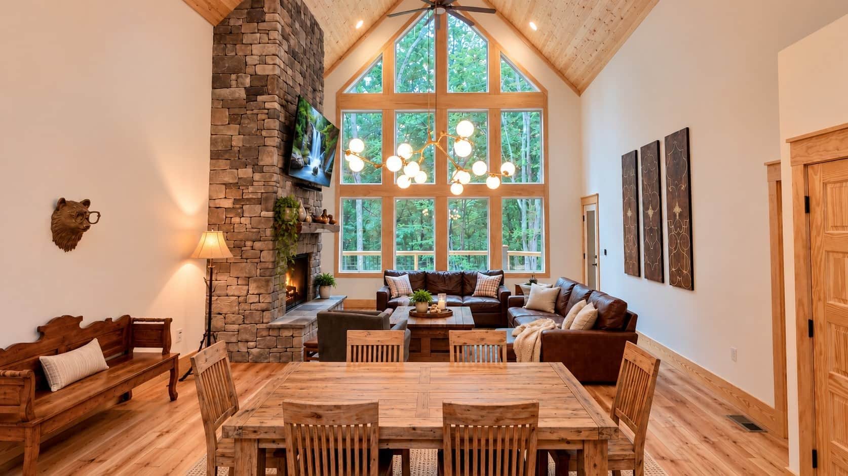 A cozy interior with a stone fireplace, wooden furniture, and large windows offering a view of the outdoors.