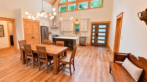 A spacious kitchen with wooden flooring, a dining table with chairs, a refrigerator, and a sink. - Celastrina Cottage of Sapphire Valley (Jackson County)