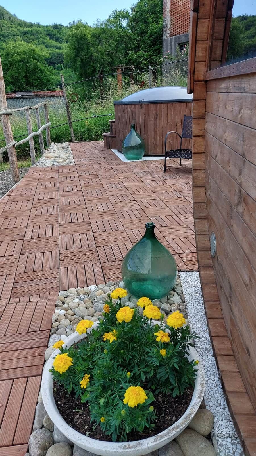 Un terrazzo in legno con un fioriere di fiori gialli, un vaso verde e una panchina.