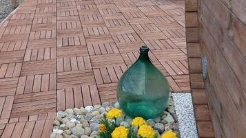 Un terrazzo in legno con un fioriere di fiori gialli, un vaso verde e una panchina.