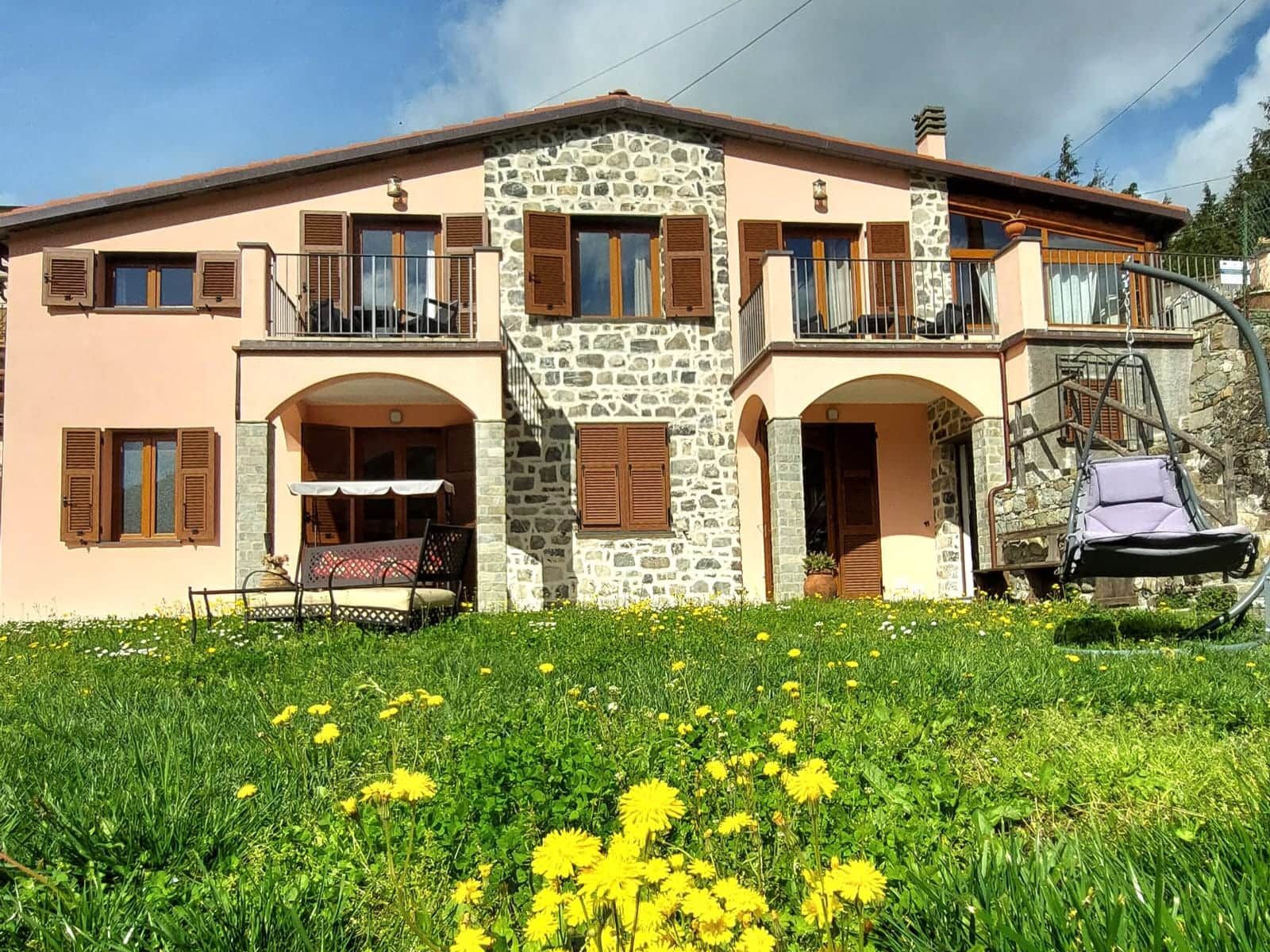 Un edificio su due piani con facciata in pietra, diverse finestre con persiane e un balcone.