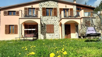 Un edificio su due piani con facciata in pietra, diverse finestre con persiane e un balcone.
