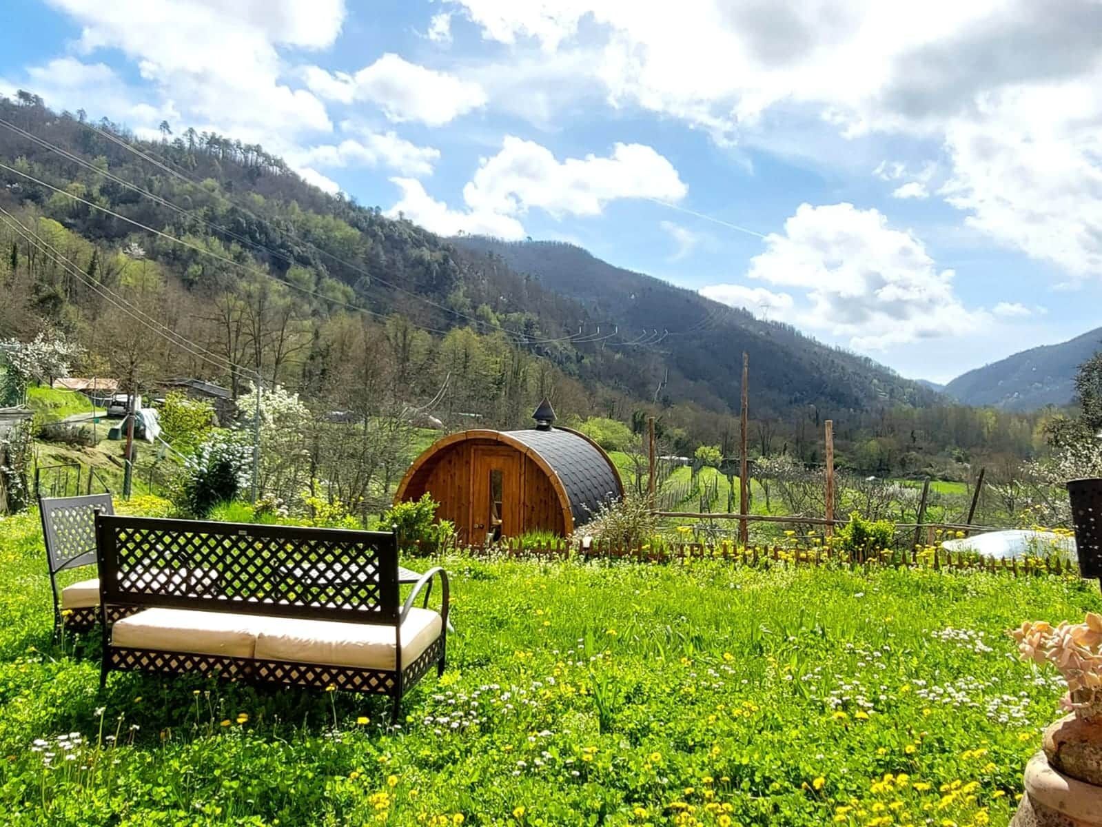 Une cabane en bois, dotée d’un toit incurvé, est entourée d’une prairie verdoyante et luxuriante, avec des montagnes en toile de fond.