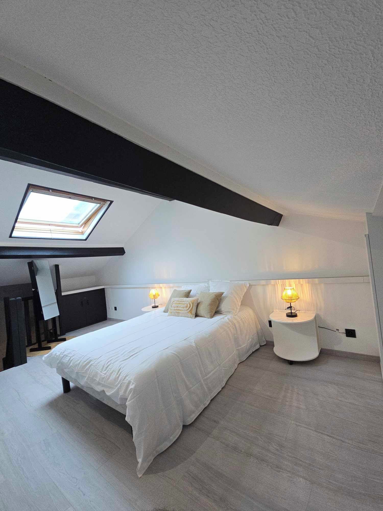 Een moderne slaapkamer met dakraam, een bed met wit beddengoed en een nachtkastje met lamp.