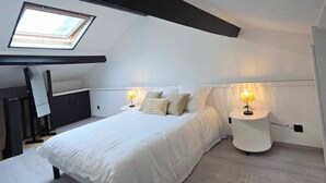 Een moderne slaapkamer met dakraam, een bed met wit beddengoed en een nachtkastje met lamp.