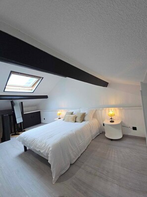 A modern bedroom with a skylight, a bed with white bedding, and a bedside table with a lamp. - New apartment near the Outlet Village (La Verpillière)