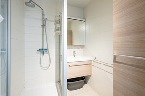 A modern bathroom with a glass shower enclosure, a white sink, and a wooden vanity. - Apartment on Zeedijk With North Sea Views (Blankenberge)
