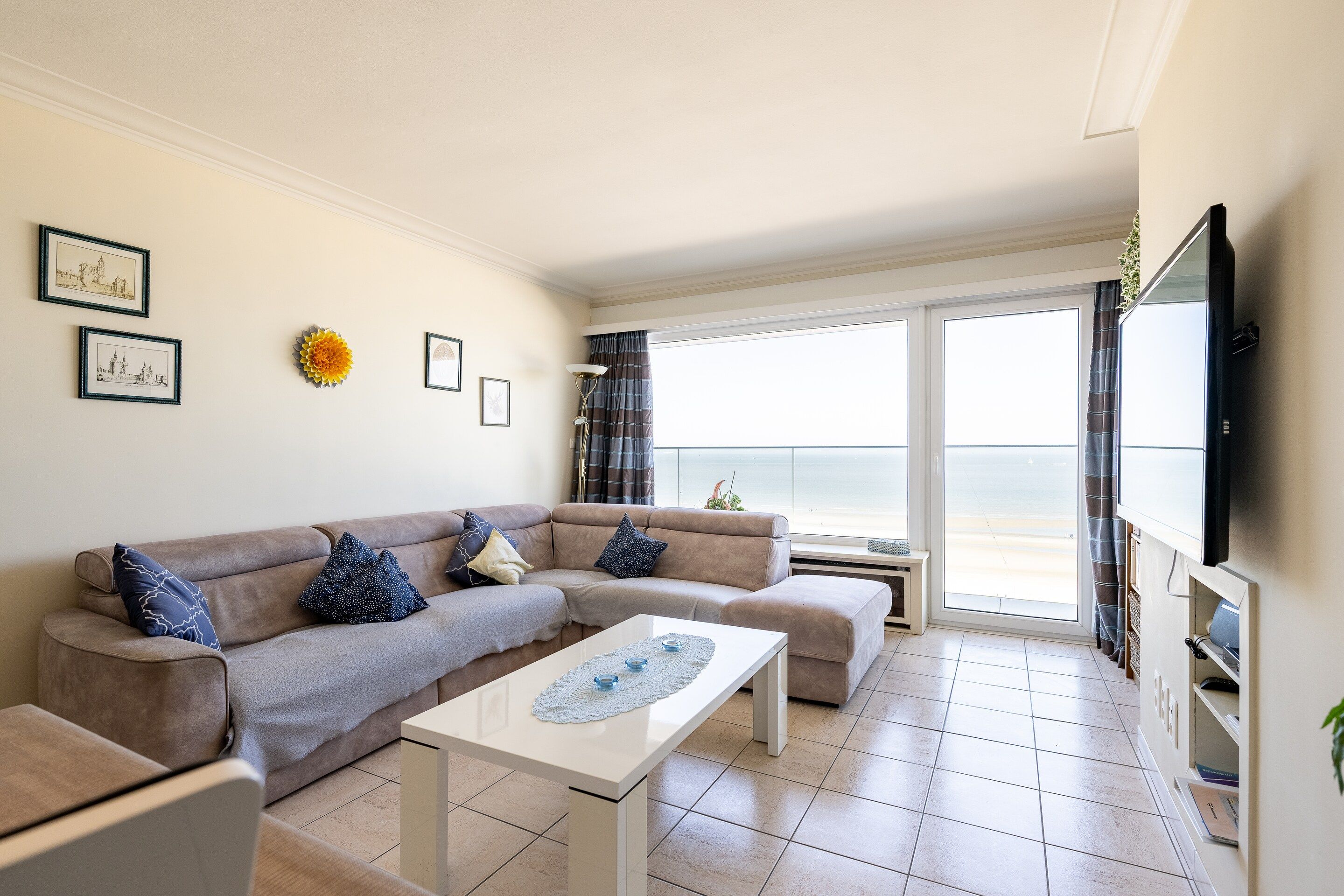A living room with a sofa, coffee table, and a view of the sea through large windows.