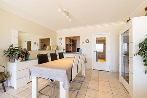 A dining area with a table, chairs, and a kitchen in the background. - Apartment on Zeedijk With North Sea Views (Blankenberge)