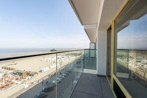 A balcony with a clear view of the beach, a parking area, and a distant cityscape. - Apartment on Zeedijk With North Sea Views (Blankenberge)