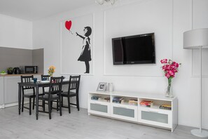 Ein zeitgemäßer Wohnbereich mit Essplatz, einem an der Wand montierten Flachbildfernseher und einem weißen Konsolentisch mit Büchern.