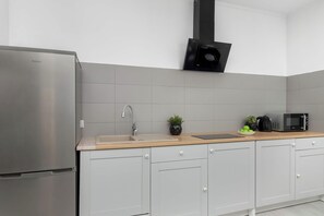 A modern kitchen with grey cabinetry, a stainless steel refrigerator, a black microwave, and a wooden countertop. - Apartament z Balkonem na 10 Pietrze w Lodzi by Noclegi Renters (Łódź)
