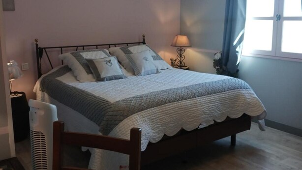 Un dormitorio con cama, mesita de noche, lámpara y ventana con cortinas.