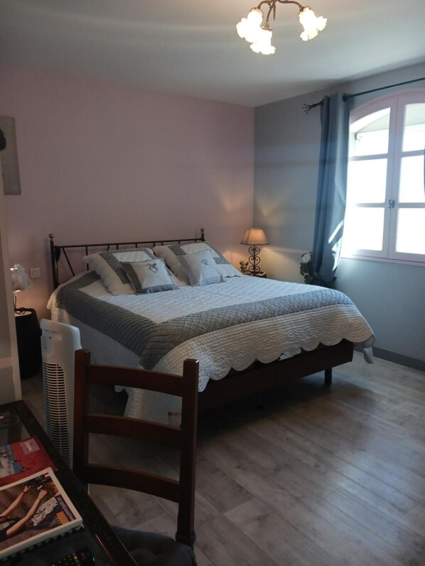 Une chambre à coucher avec un lit, une table de chevet, une lampe et une fenêtre avec des rideaux.