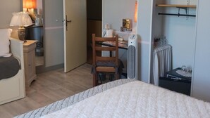 Un dormitorio con cama, escritorio, silla, armario y mesita de noche.