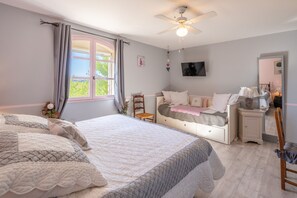 A bedroom with two beds, a ceiling fan, a TV, and a window with curtains.