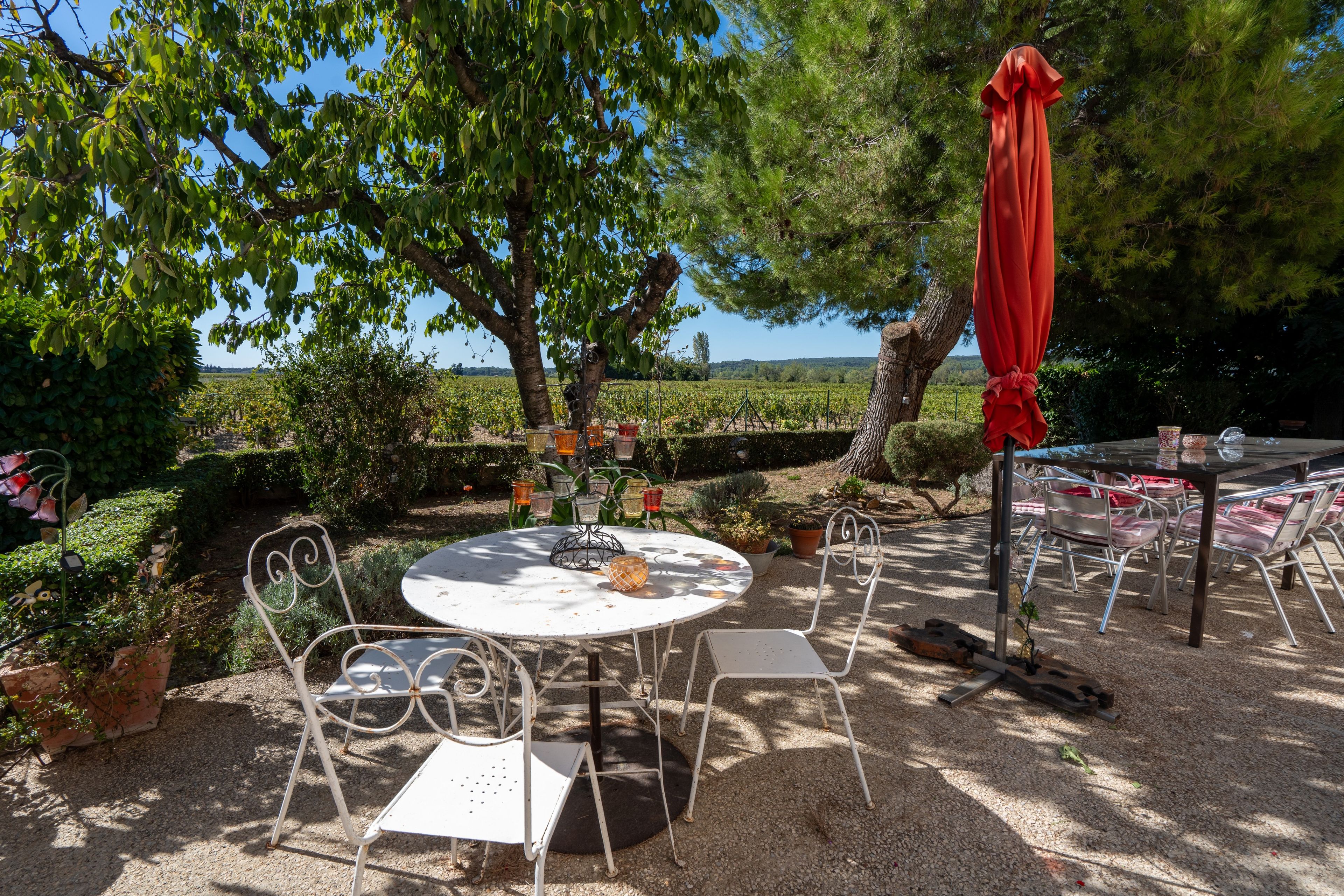 An outdoor seating area with a round table and chairs, surrounded by greenery and a view of the landscape.