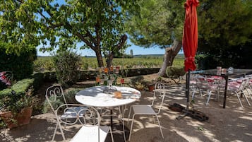 An outdoor seating area with a round table and chairs, surrounded by greenery and a view of the landscape.