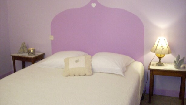 Un dormitorio con una cama, dos mesitas de noche, una lámpara y un adorno en la pared.