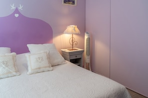 A neatly made bed with white bedding and decorative pillows, a bedside table with a lamp, and a wall-mounted heater. - Room 'Chambre Syrah' with Mountain View, Shared Pool and Wi-Fi (Sainte-Cécile-les-Vignes)