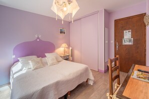 A bedroom with a bed, bedside tables, a lamp, a chair, a wooden door, and a wall-mounted light fixture.