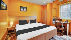 Een hotelkamer met een bed, een bureau, een stoel, een kledingkast, een raam en een plafondventilator.