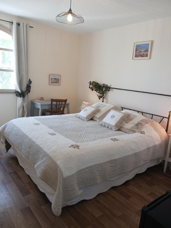 Une chambre à coucher avec un grand lit, une petite table, une chaise, un luminaire suspendu et un tableau encadré au mur.