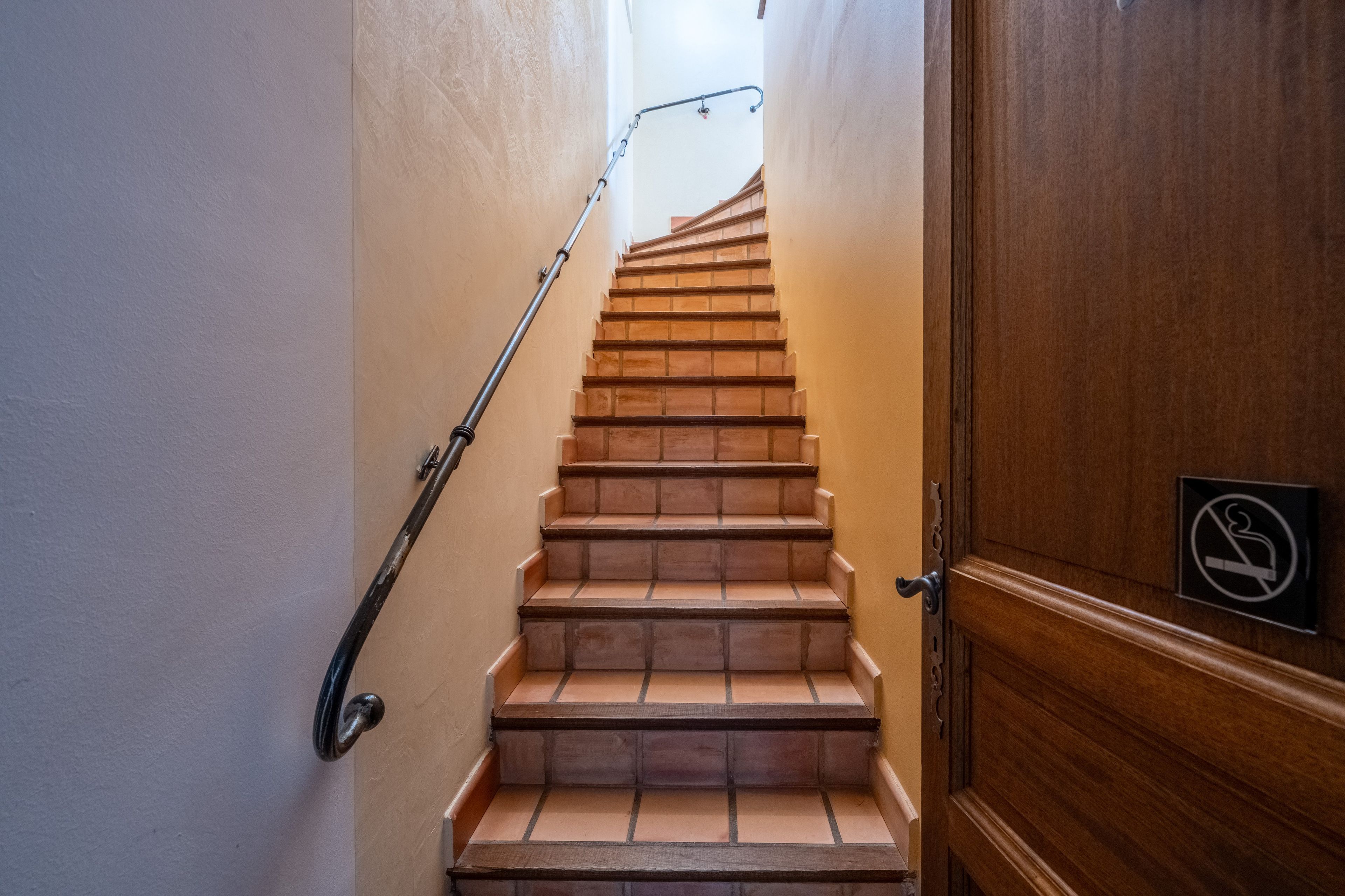 Eine Holztreppe mit Handlauf führt zu einer Tür, an der ein Rauchverbotsschild angebracht ist.