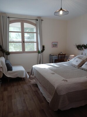 Une chambre à coucher avec un grand lit, un bureau, une chaise, une fenêtre avec des rideaux et un luminaire suspendu.