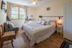 Une chambre à coucher avec un lit, un bureau, une chaise, un ventilateur de plafond et une fenêtre avec des rideaux.