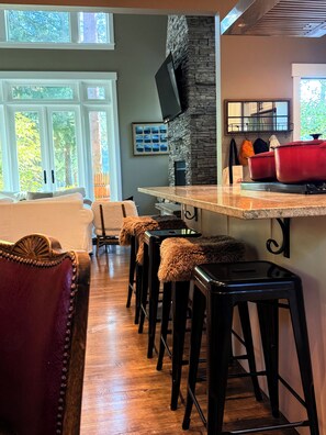 A modern kitchen with a stone fireplace, bar stools, and a red pot on the counter. - LUX home on Golf Course-hot tub-sleeps 8 (Cle Elum)