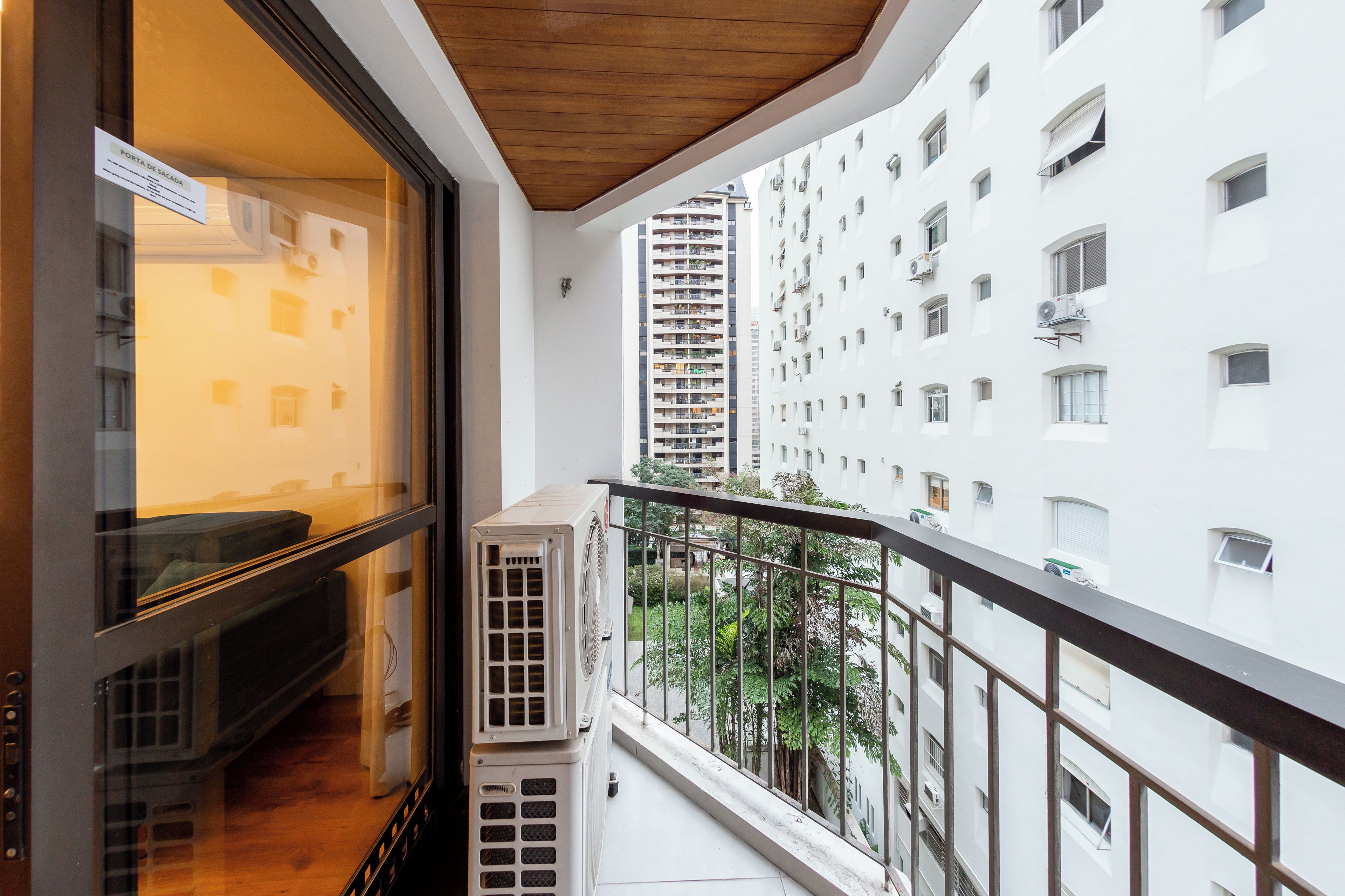 A balcony with a view of a high-rise building, a window with a sign, and an air conditioning unit.